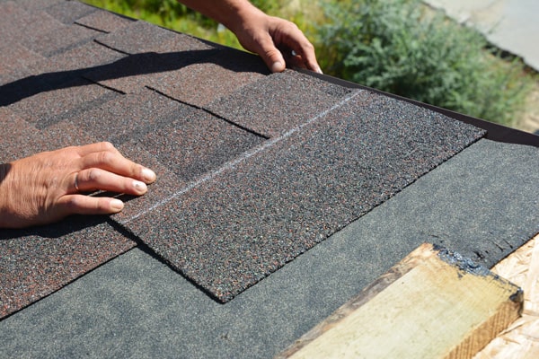 Worker installing asphalt shingles on a roof.